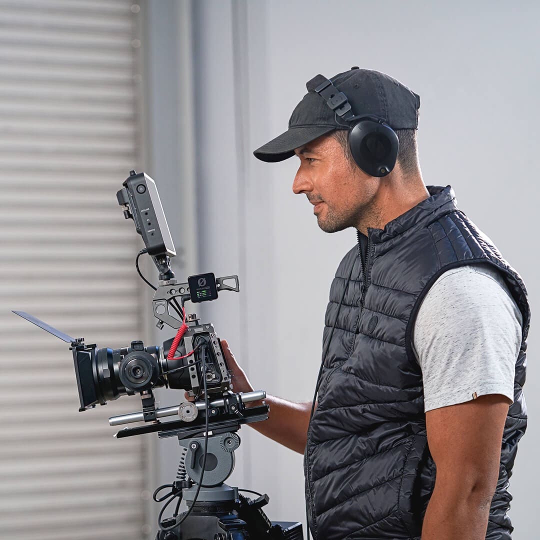 a man in a black vest and a camera with rode wireless pro