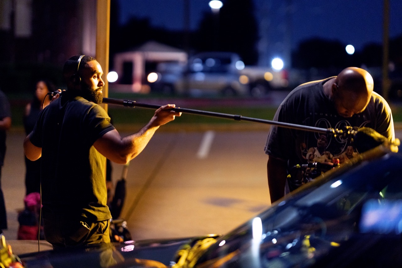 a man holding a boom pole next to the director of photography on a scripted narrative set